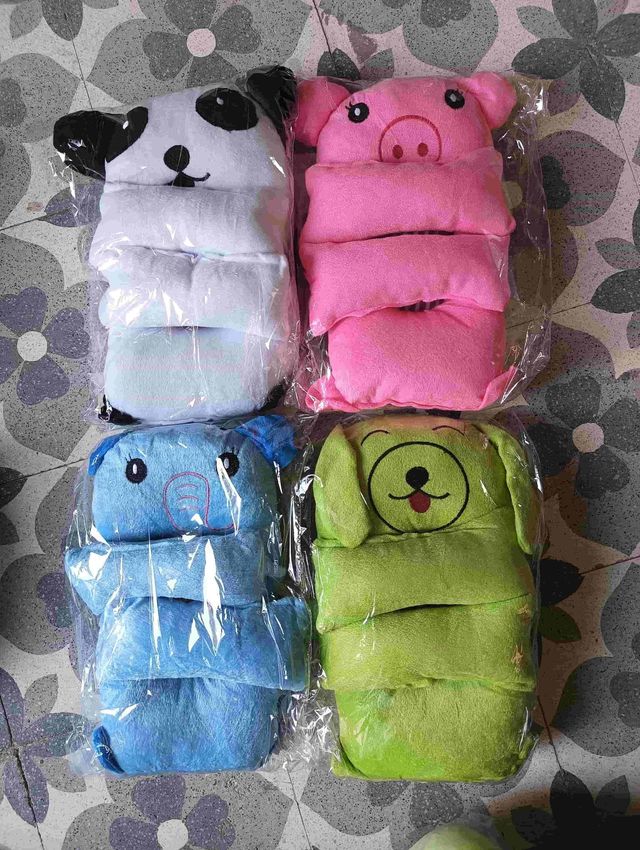 Four animal-themed baby booties in plastic packaging on a patterned surface.
