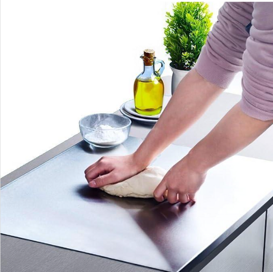 Person kneading dough on a stainless steel countertop with a bowl and oil bottle in the background.