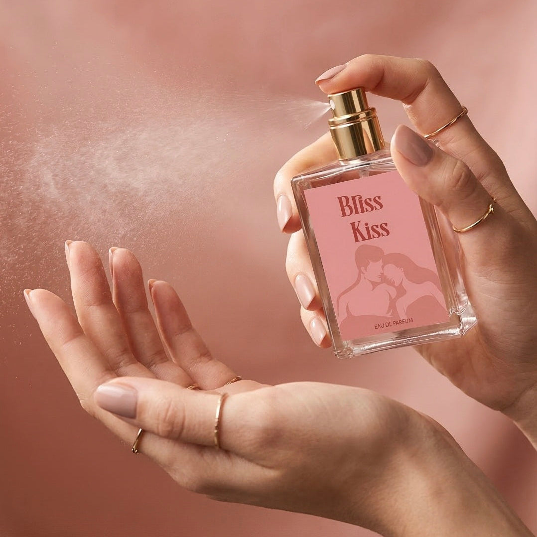 Hand holding a perfume bottle labeled 'Bliss Kiss' with a soft pink background