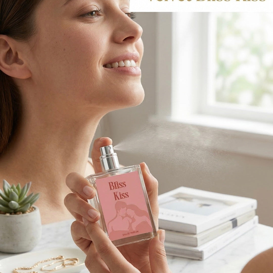 Woman holding a 'Bliss Kiss' perfume bottle in a bright room with a window in the background.