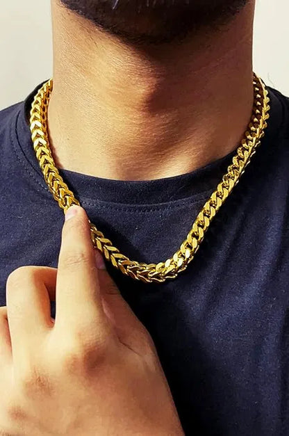 Gold chain necklace being held by a hand against a plain background