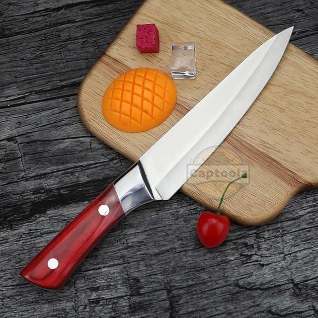 Chef's knife with a red handle on a wooden cutting board with fruits and vegetables.